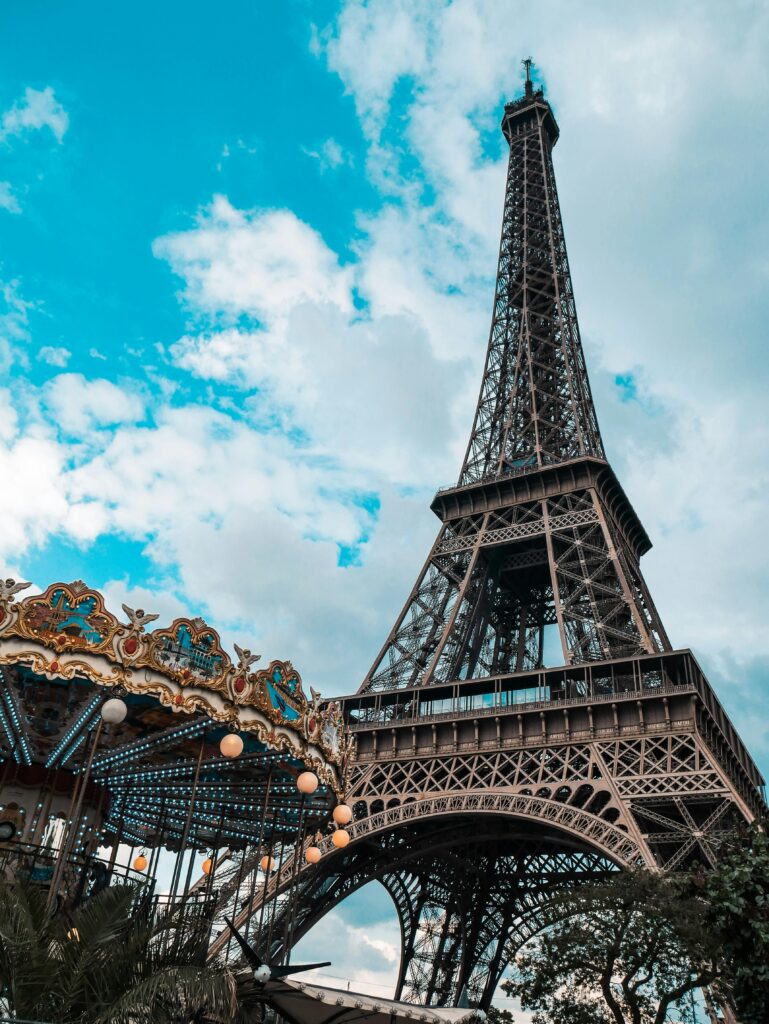Eiffel Tower in Paris with carousel in foreground under a bright blue sky.